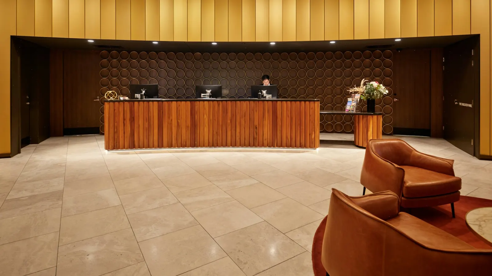 Elegant hotel lobby with a warm wood-panelled reception desk, leather lounge chairs, and a receptionist at the counter, representing the in-person luxury service guests expect to be matched online.