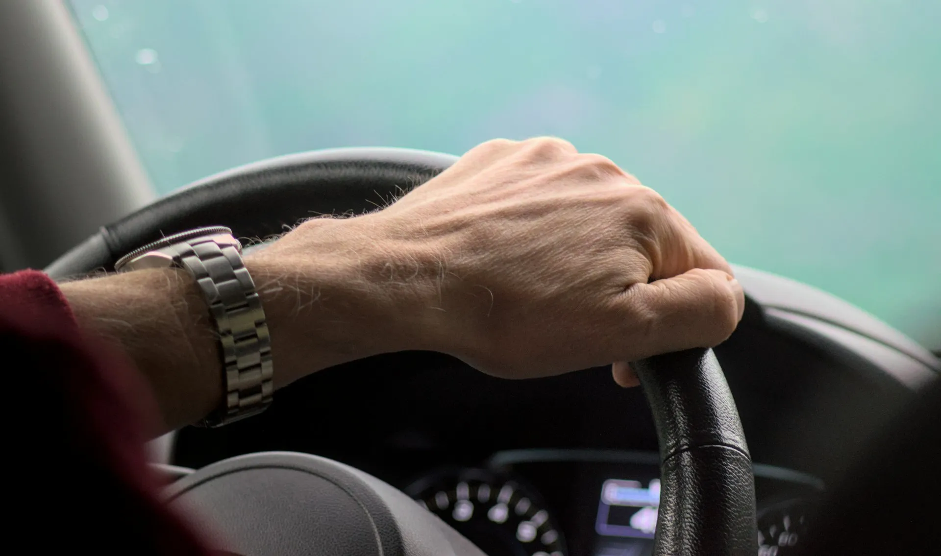 Close-up of a hand gripping a car's steering wheel while driving, representing the test-drive moment where ICE and EV shoppers alike decide whether to commit to a purchase.