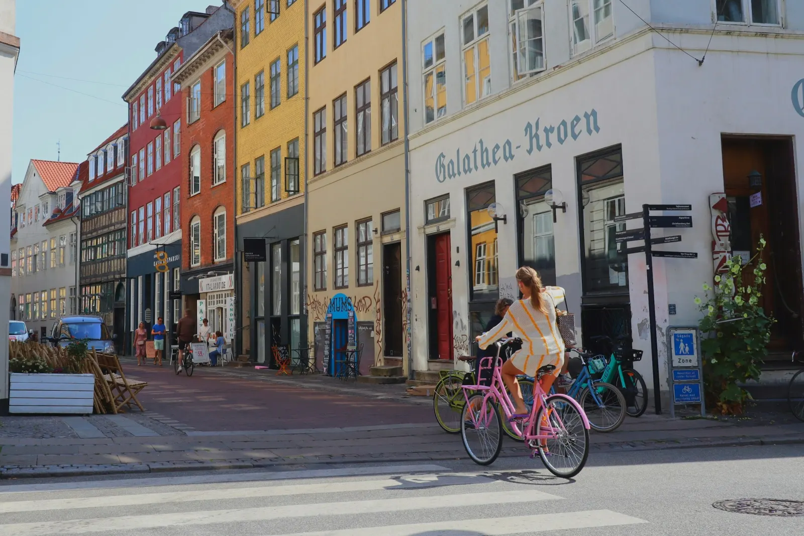 A cyclist passing colourful townhouses, a restaurant and a takeaway on a Copenhagen street, where restaurants now compete to win delivery orders directly.