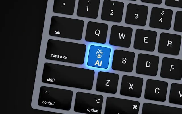 A close-up of a sleek, dark keyboard where the letter 'A' is replaced by a glowing blue key labeled 'AI' with a humanoid icon, representing the integration of artificial intelligence into daily user interactions and digital discovery.