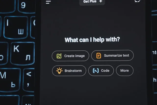A close-up of a mobile AI assistant interface (ChatGPT) displaying prompt options like 'Brainstorm' and 'Summarize text' held over a dark backlit keyboard, illustrating the shift from traditional search to AI-driven brand discovery.
