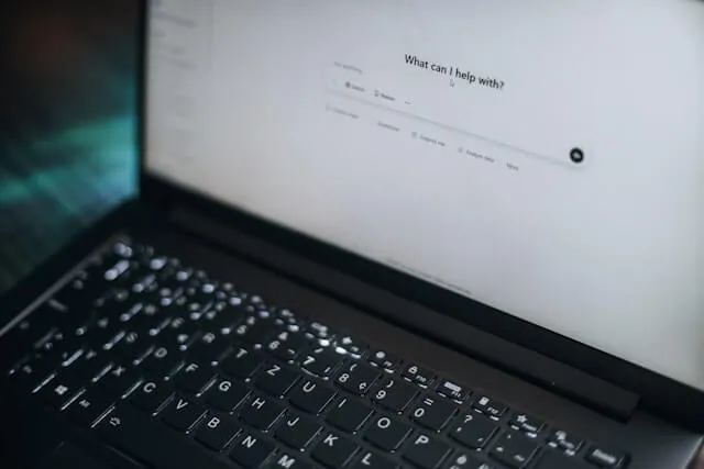 A side-profile view of a laptop screen displaying the ChatGPT 'What can I help with?' interface, highlighting the transition from traditional search engines to conversational AI assistants for desktop users.