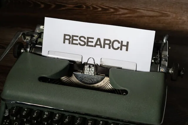 A vintage green typewriter with a white sheet of paper featuring the word 'RESEARCH' printed in bold, capital letters, symbolizing the foundational and empirical nature of UX research and data-driven product strategy.